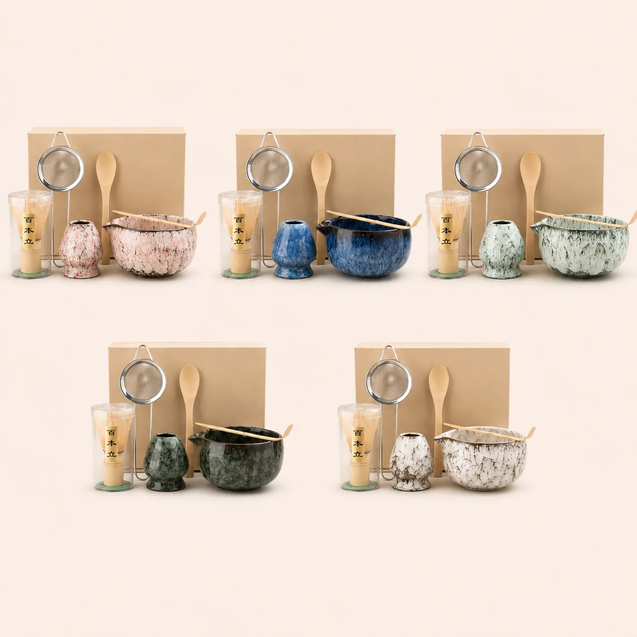 Five complete matcha sets in pink, blue, seafoam, dark green and speckled white glazes grouped together on a cream background, each with a kraft gift box, ceramic bowl, whisk holder, bamboo whisk, sifter and spoon