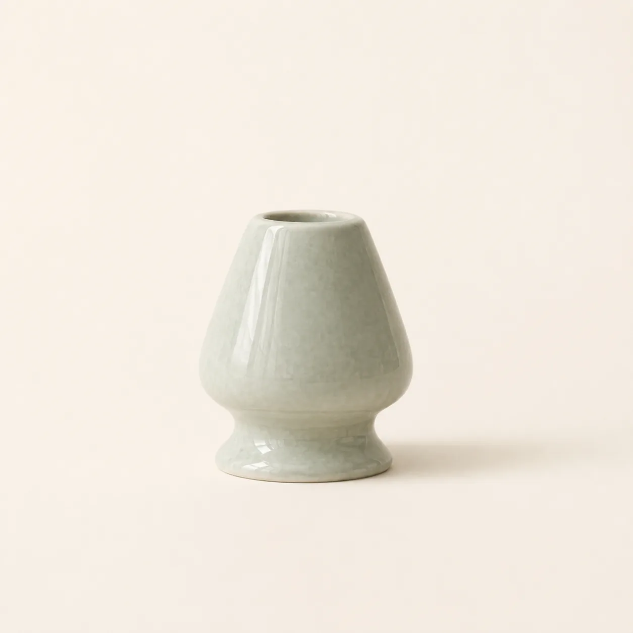 A single sage green glazed ceramic matcha whisk holder standing on a plain cream background