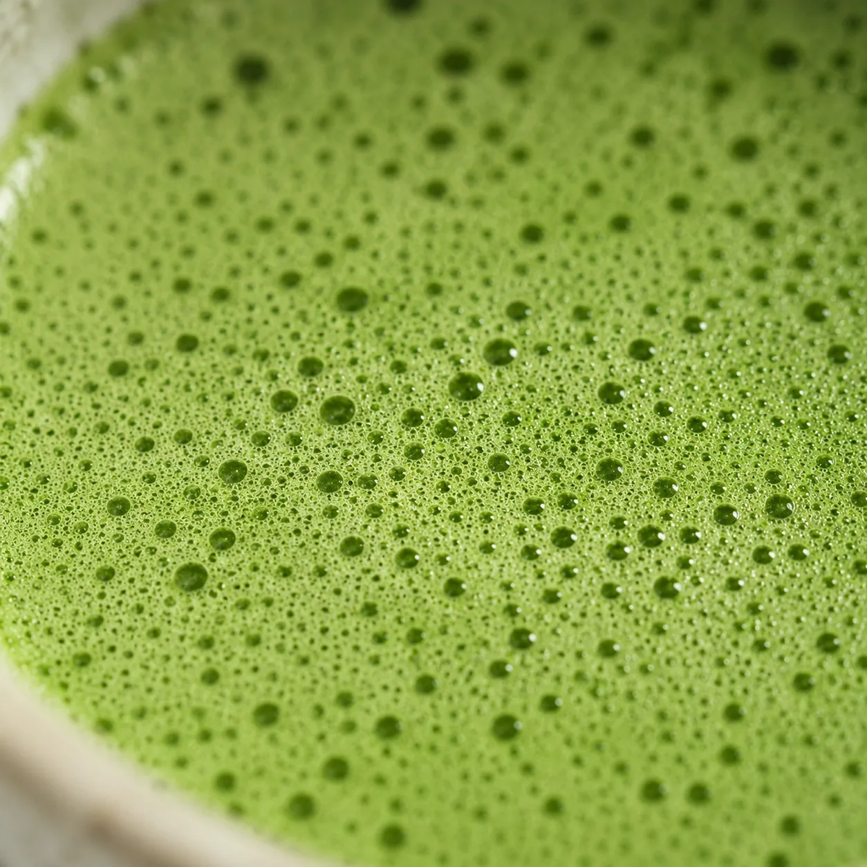 Close-up of the dense, fine foam on freshly whisked matcha, its bright green surface covered in tiny even bubbles