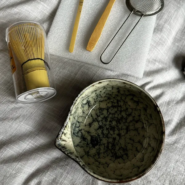 Speckled white matcha set laid out on linen in daylight: spouted bowl, whisk in its case, scoop, teaspoon and sieve, customer photo