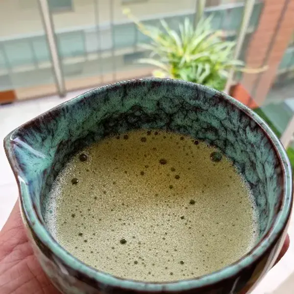 Freshly whisked matcha with a fine foam layer, held in a customer hand