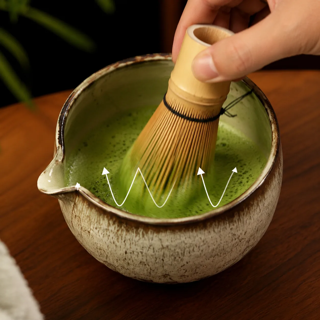 Whisking matcha to a froth with a bamboo chasen in a ceramic bowl